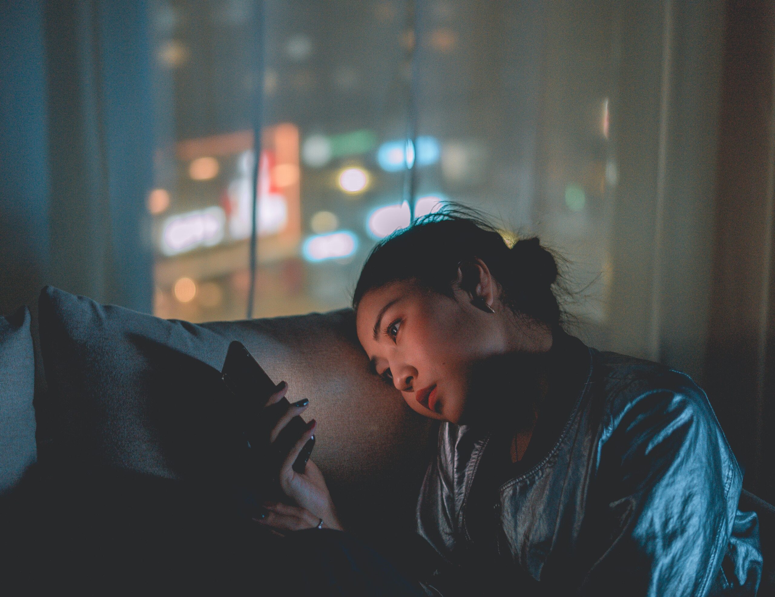 An asian woman scrolling her phone in her dark apartment, looking bored